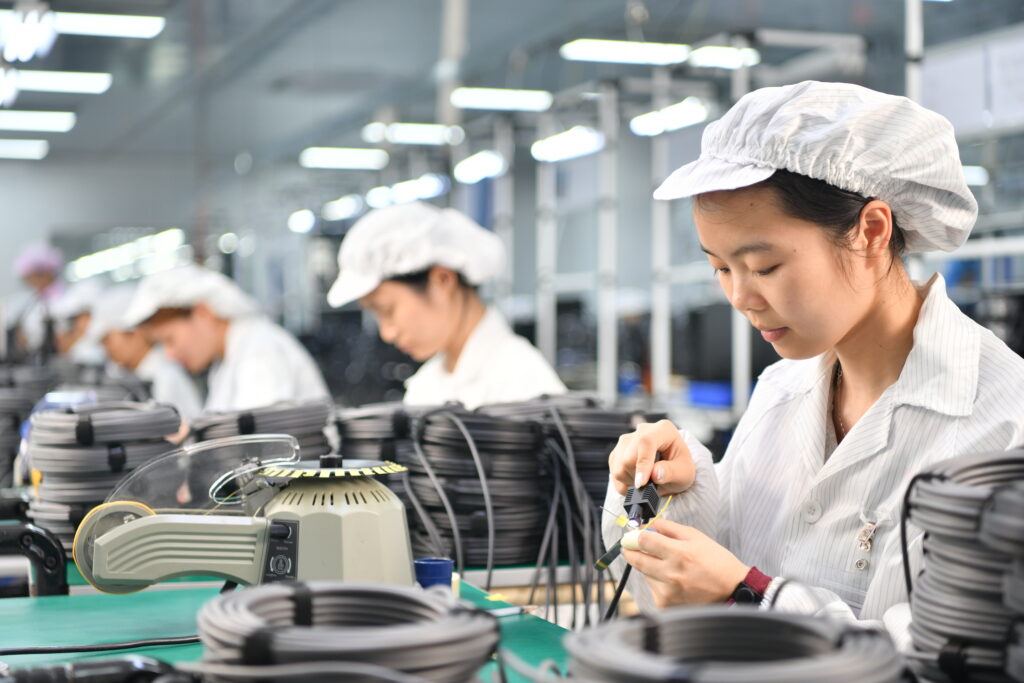 Worker assembling a cable connector alongside coiled cables on a factory production line.